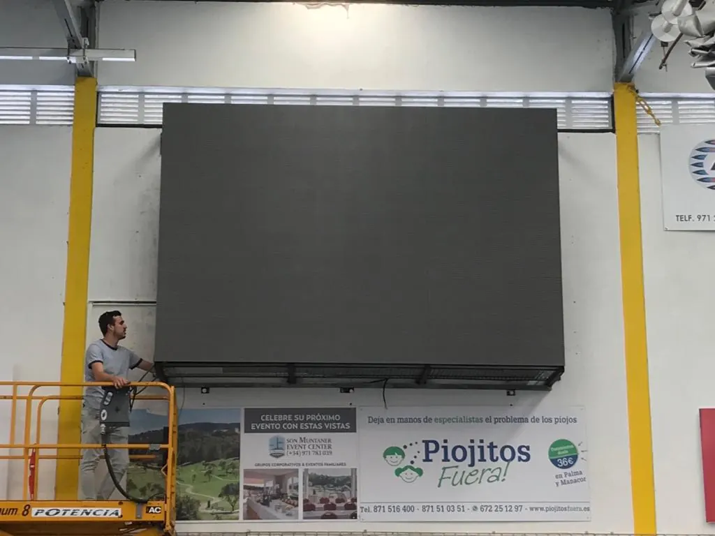 Technicien sur une nacelle élévatrice à côté de l'écran LED de la salle